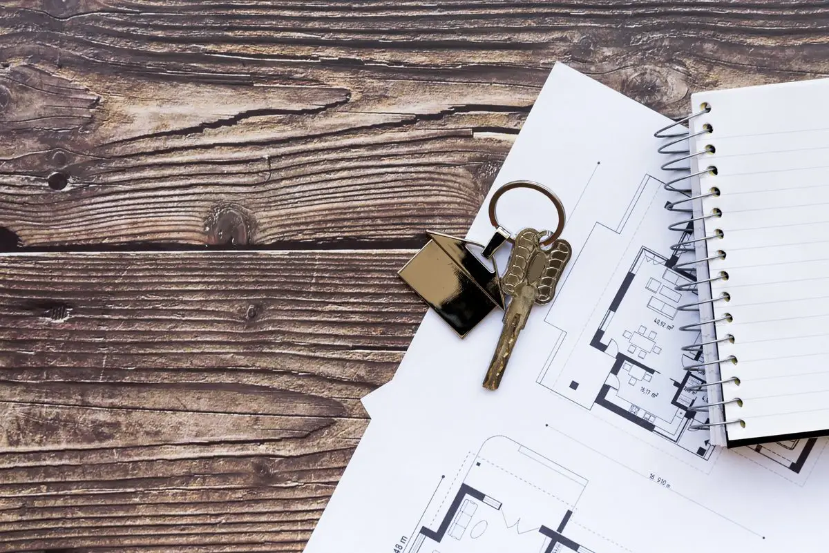House keys resting on a floor plan beside a spiral notebook