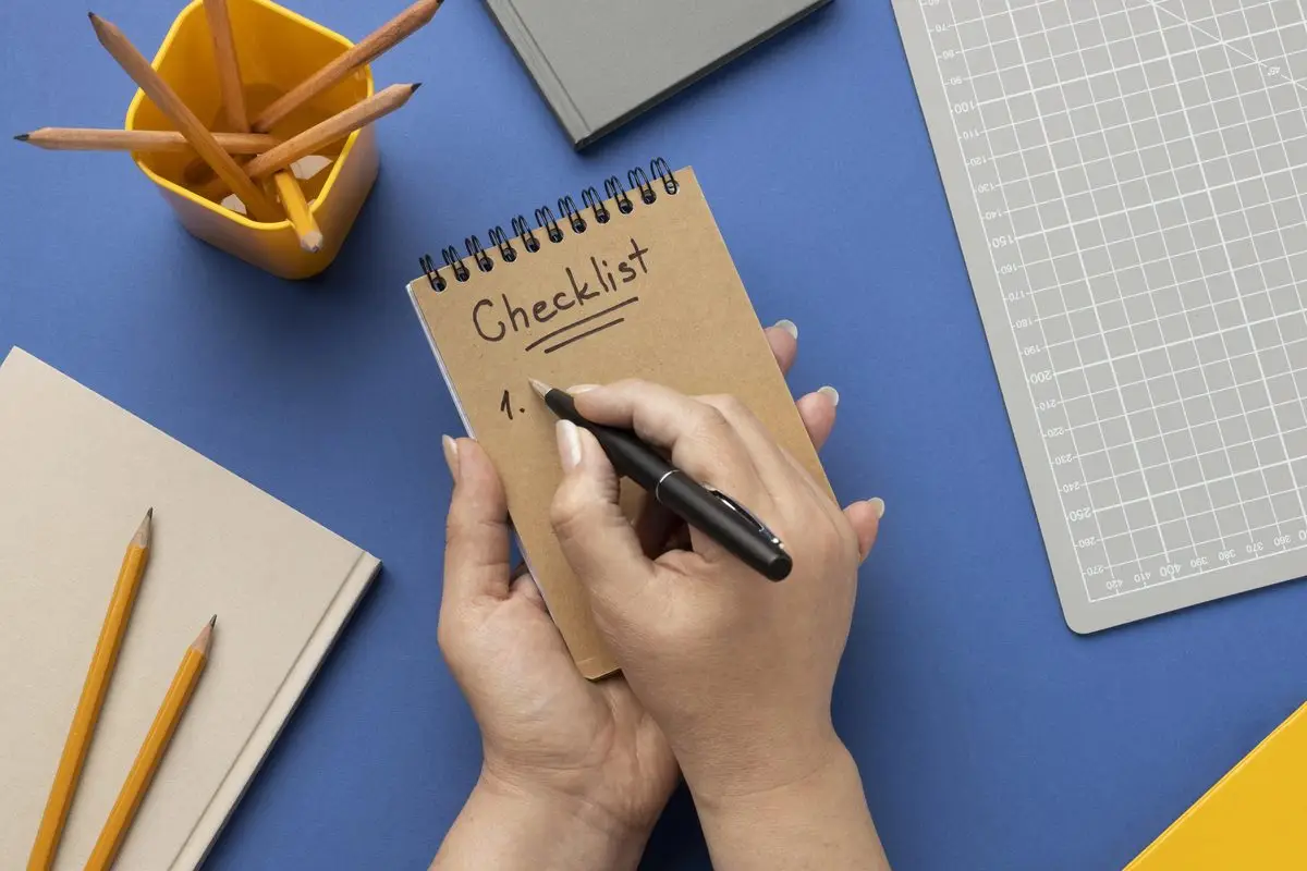 Hands writing a checklist in a spiral notebook on a desk