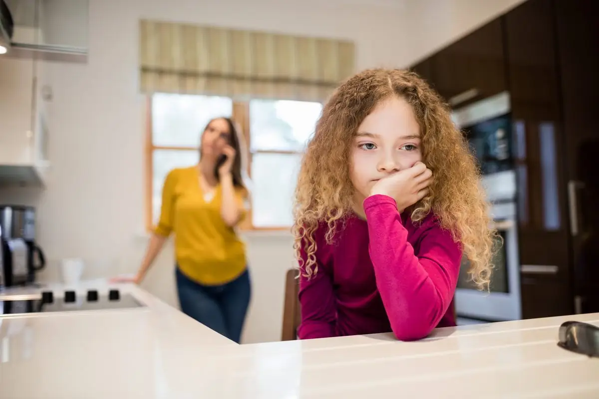 An upset child sitting on the stairs with a parent in the background