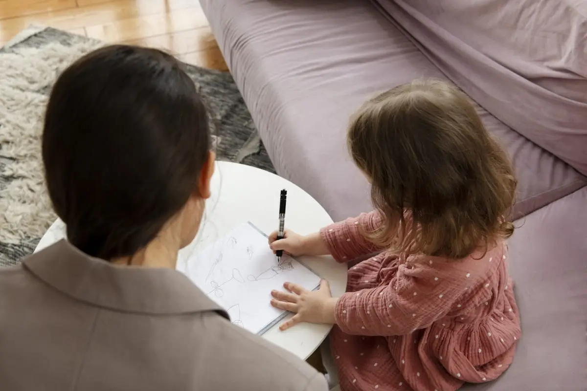 A child drawing and talking with a counsellor while an adult listens
