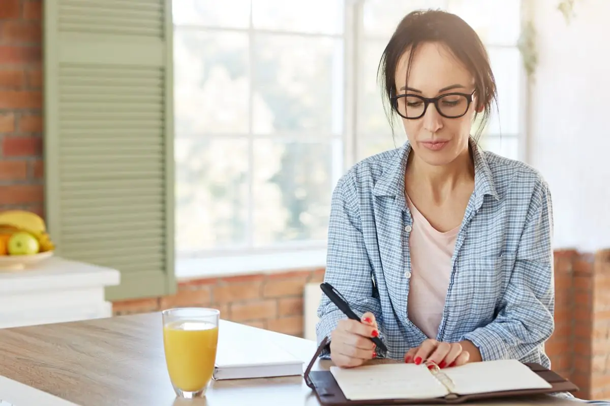 A parent writing questions in a notebook at the kitchen table before a meeting