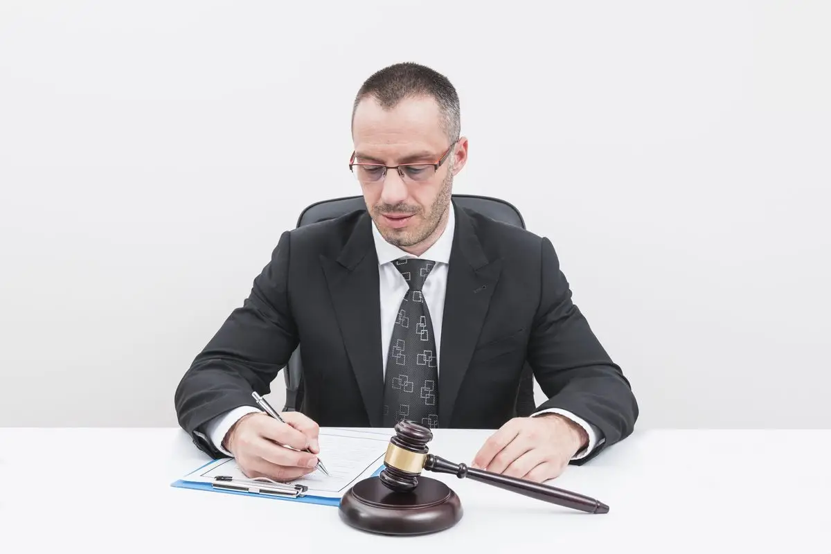 A lawyer filling in a court document at a desk beside a gavel