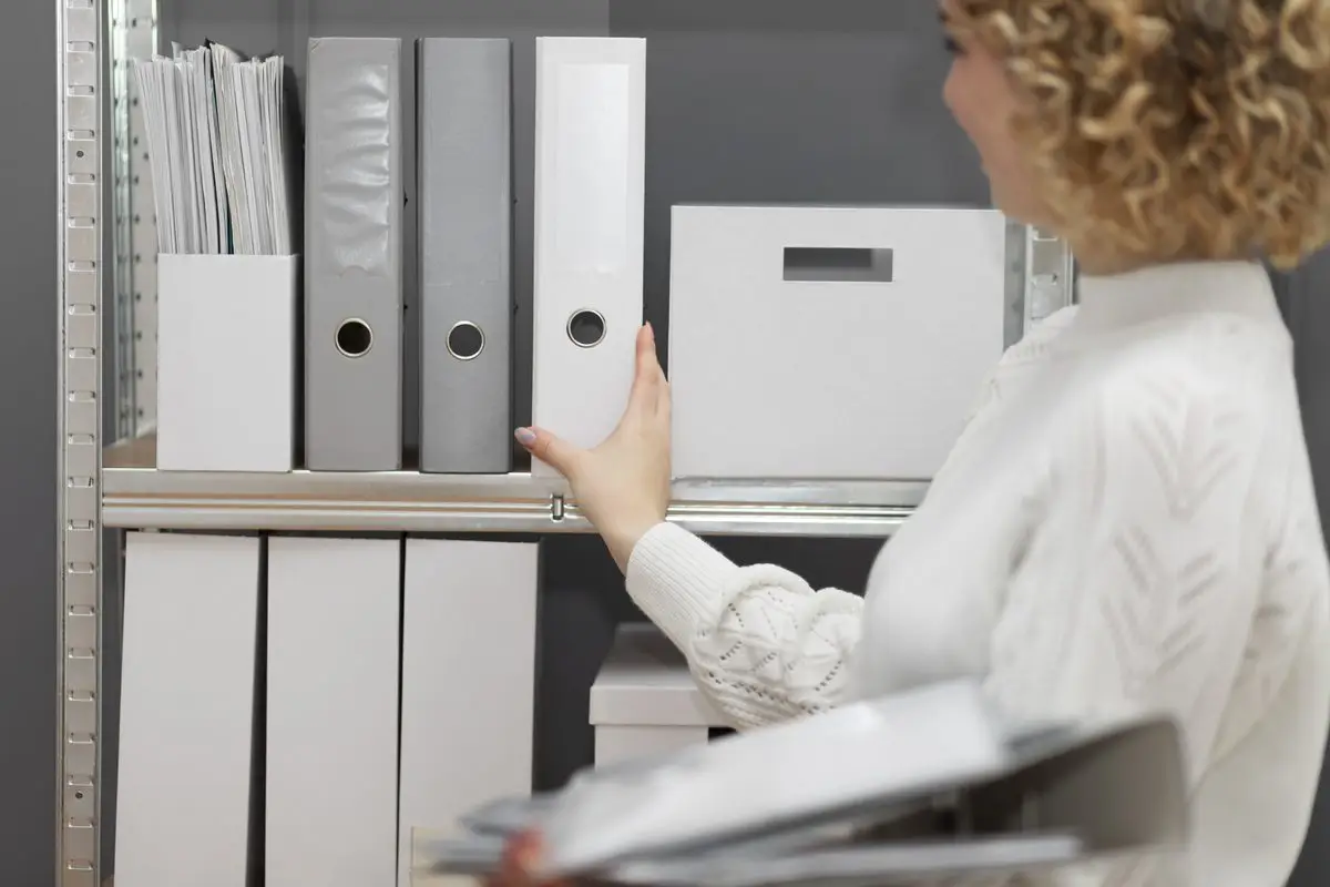 A person sorting folders of papers on a shelf to prepare evidence