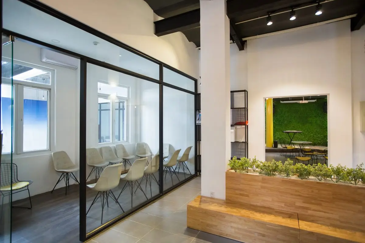 A bright, modern office with glass-walled meeting rooms and a seating area