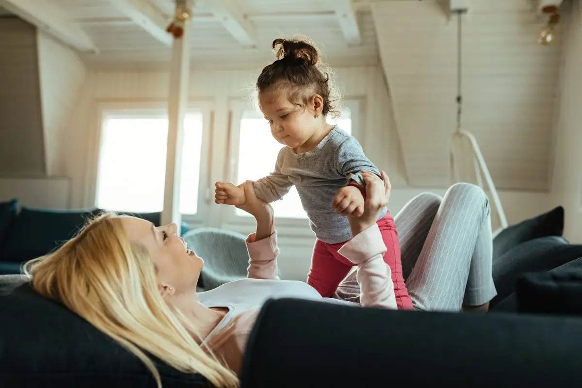 A mother lying on a sofa playing with her toddler daughter