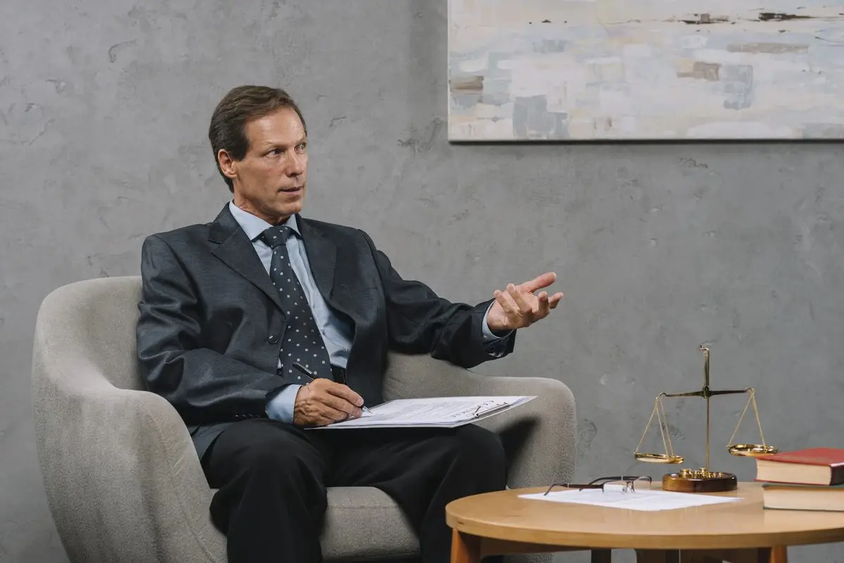 A lawyer in a suit speaking from an armchair in front of scales of justice