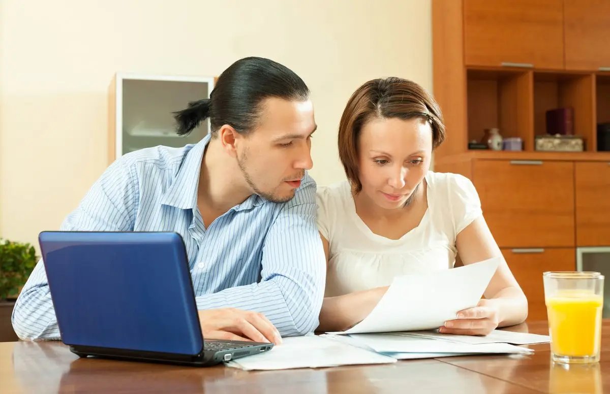 A couple going through papers at a table beside a laptop