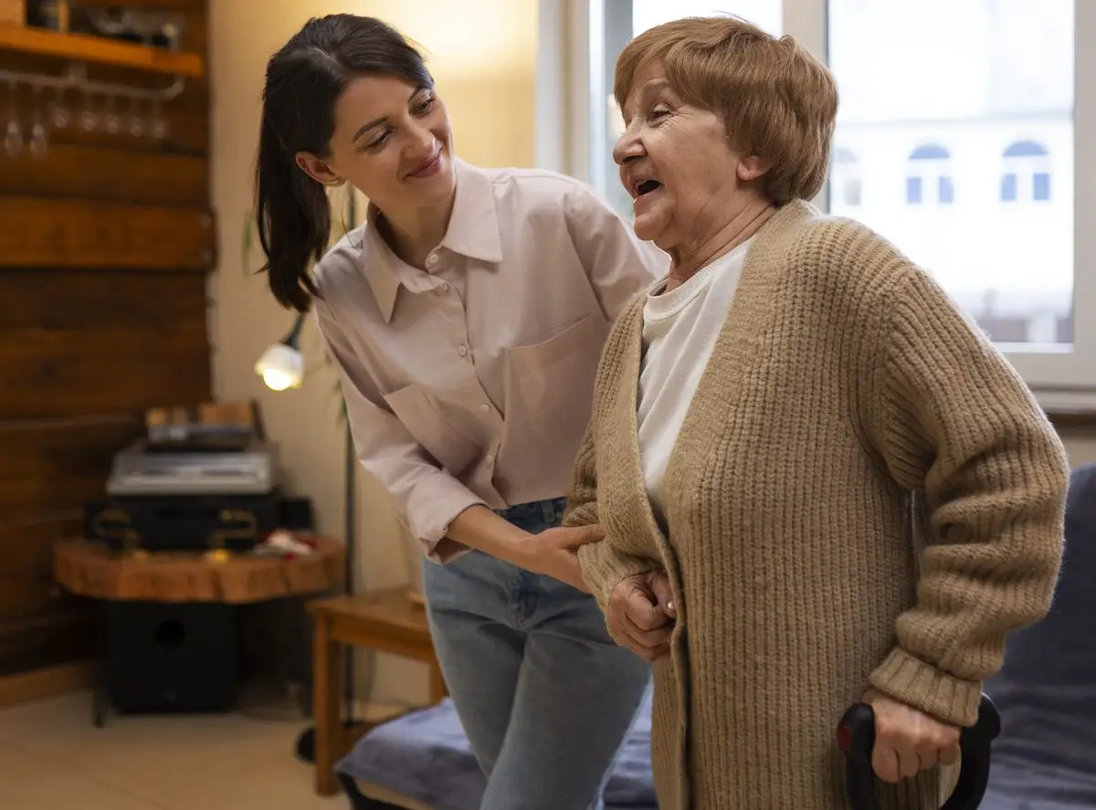 A home caregiver helping an older woman walk across her living room