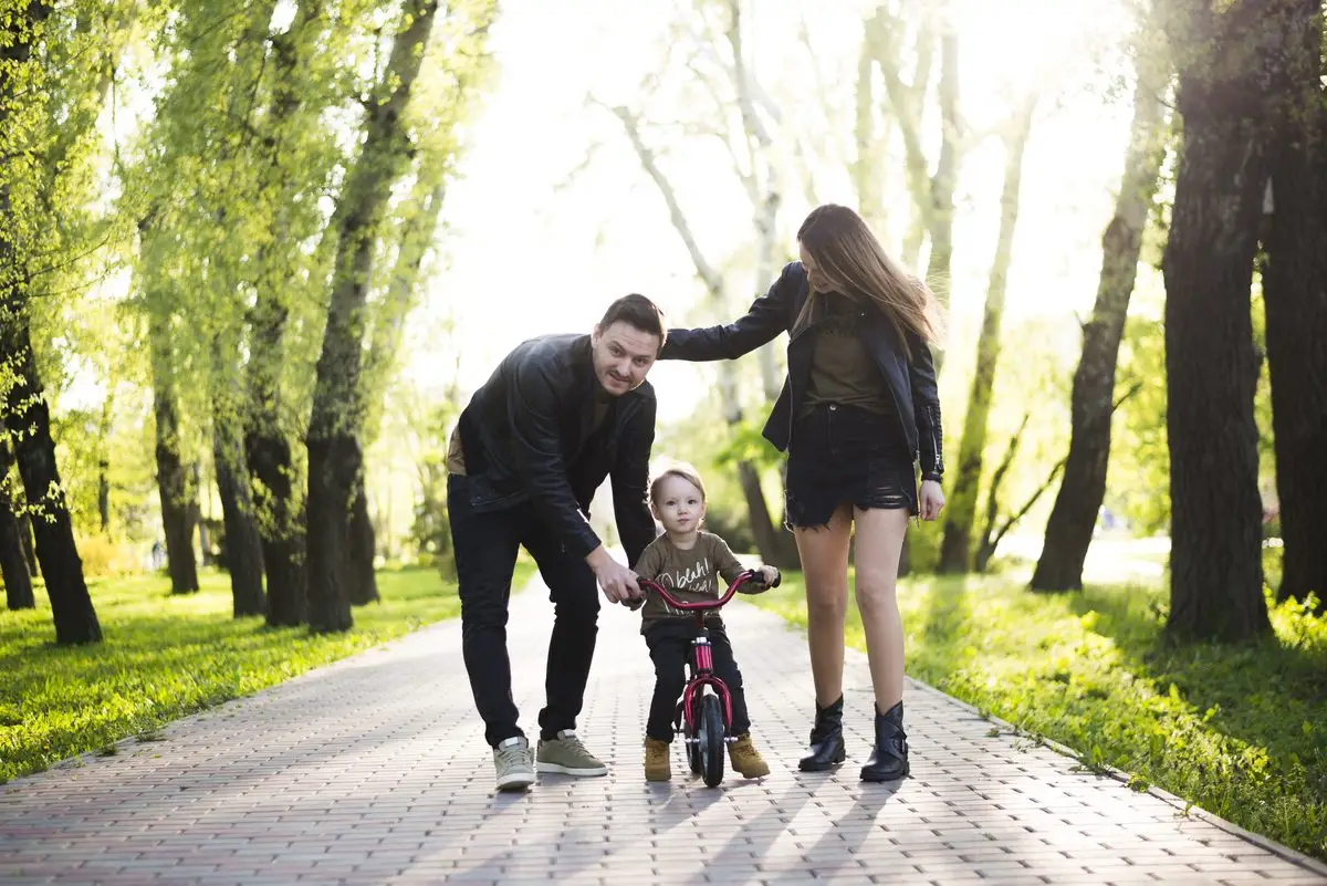 Two parents helping their small child learn to ride a bike in a park