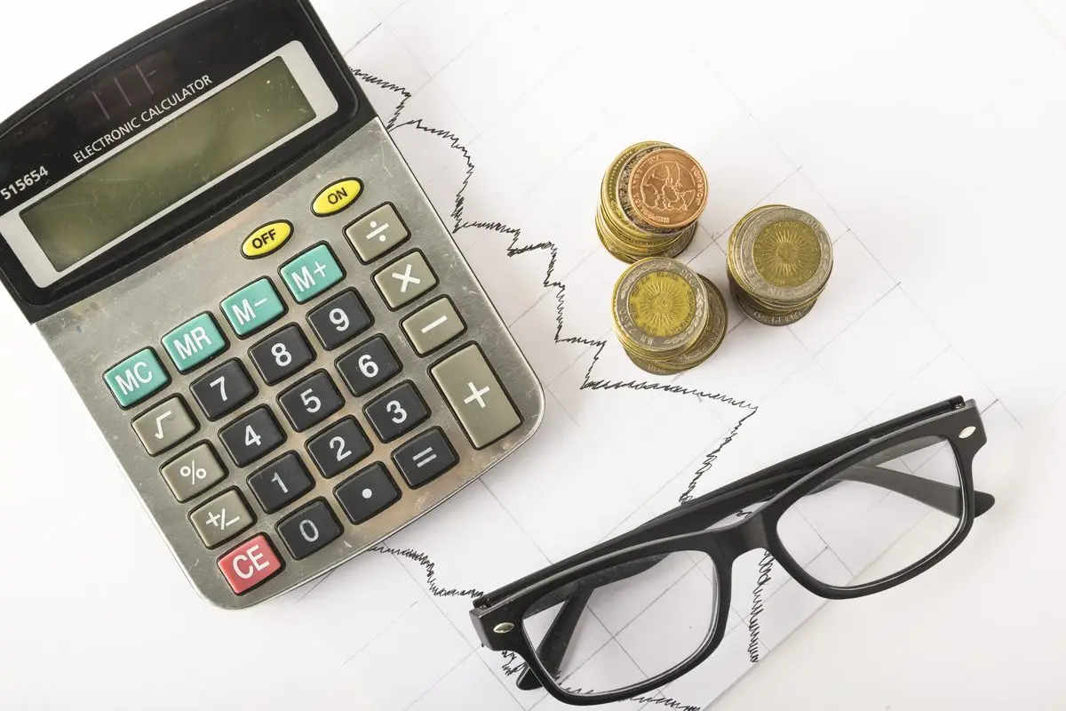 A calculator, coins and reading glasses on a desk