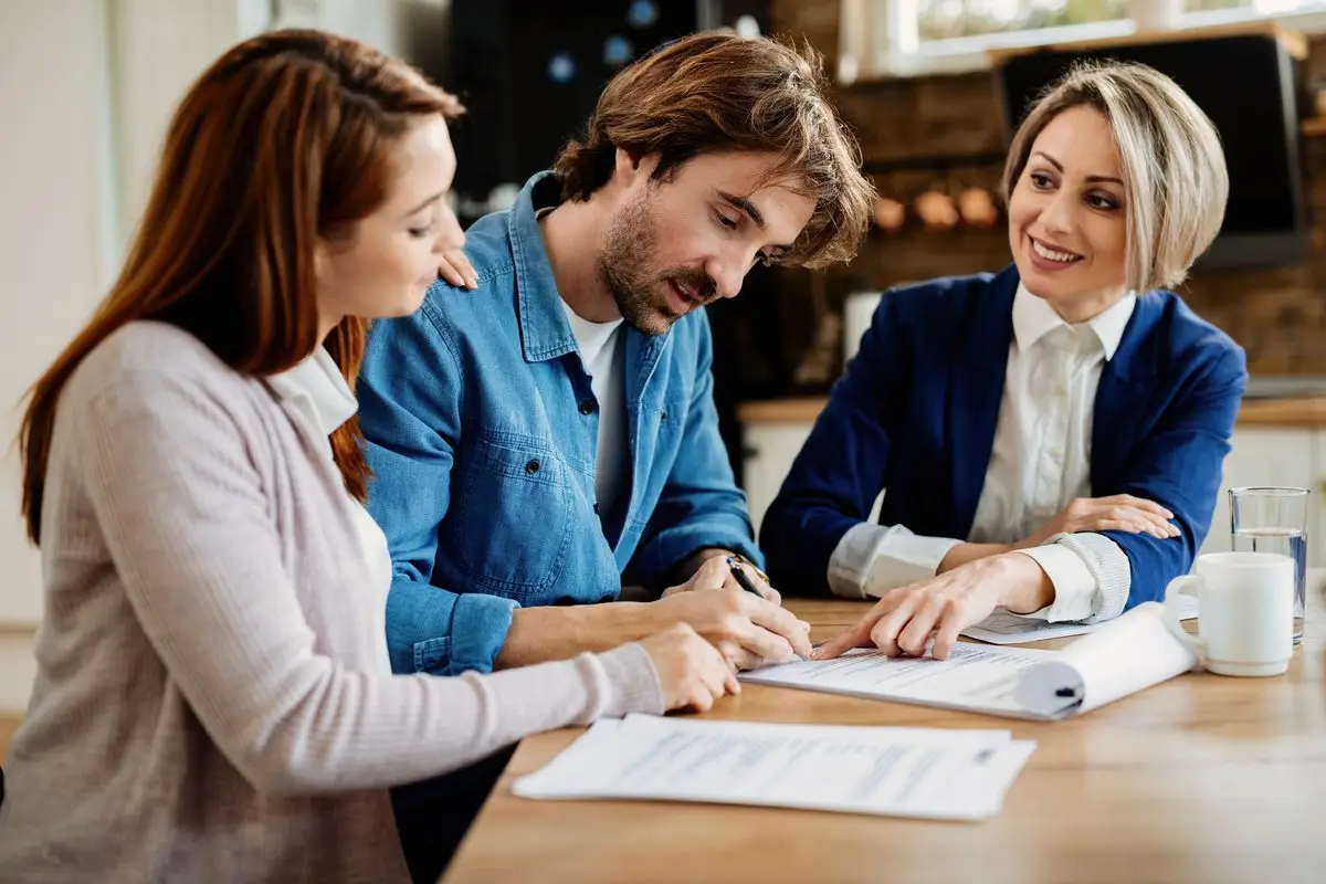 A couple signing an agreement at a table with an adviser