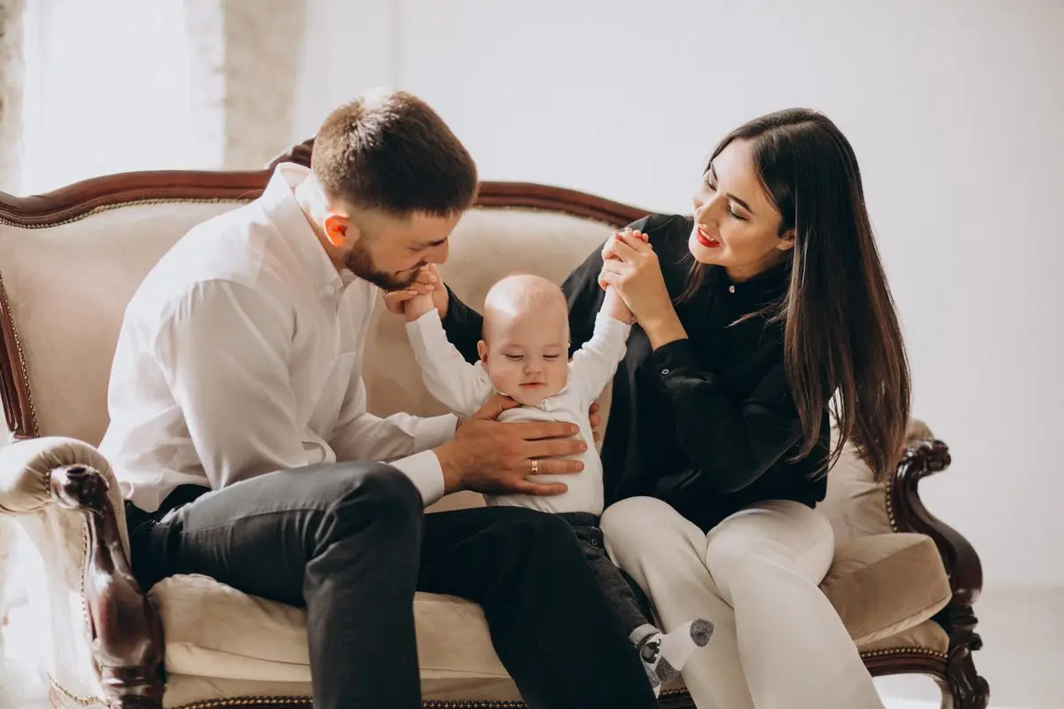 Two parents sitting on a sofa at home with their baby