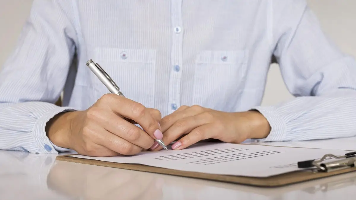 A person signing a document on a clipboard at a desk