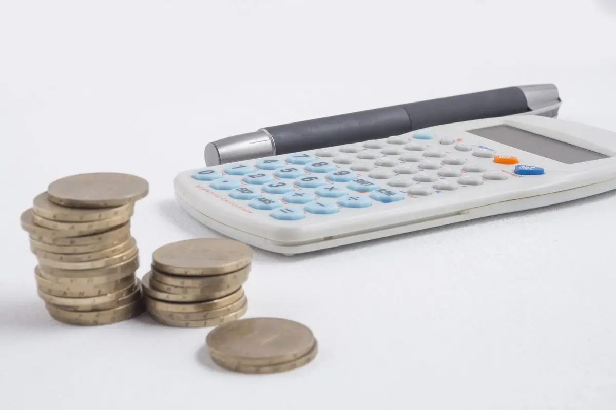 Stacks of coins beside a calculator and a pen
