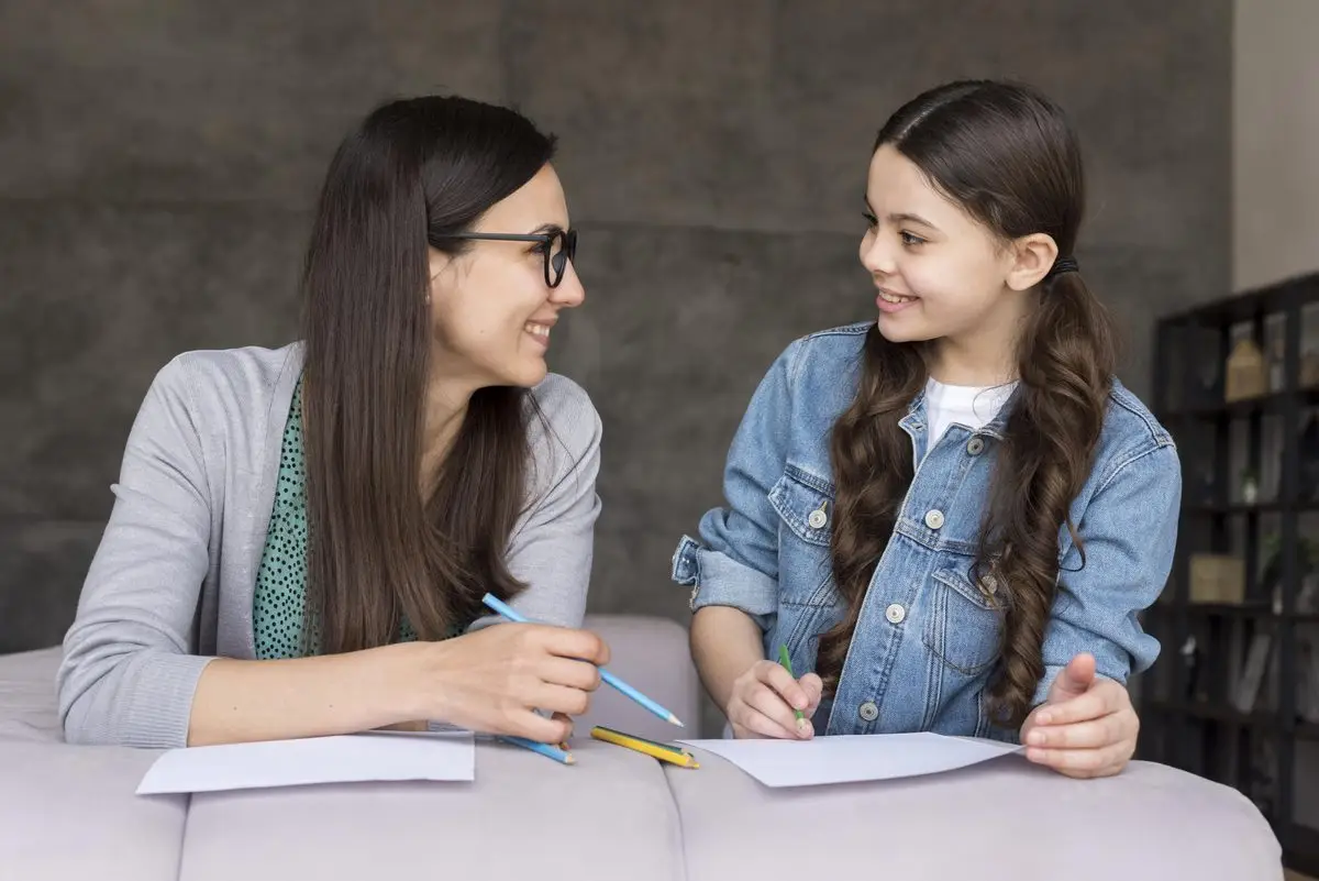 A mother and her daughter sit side by side at a table, drawing together