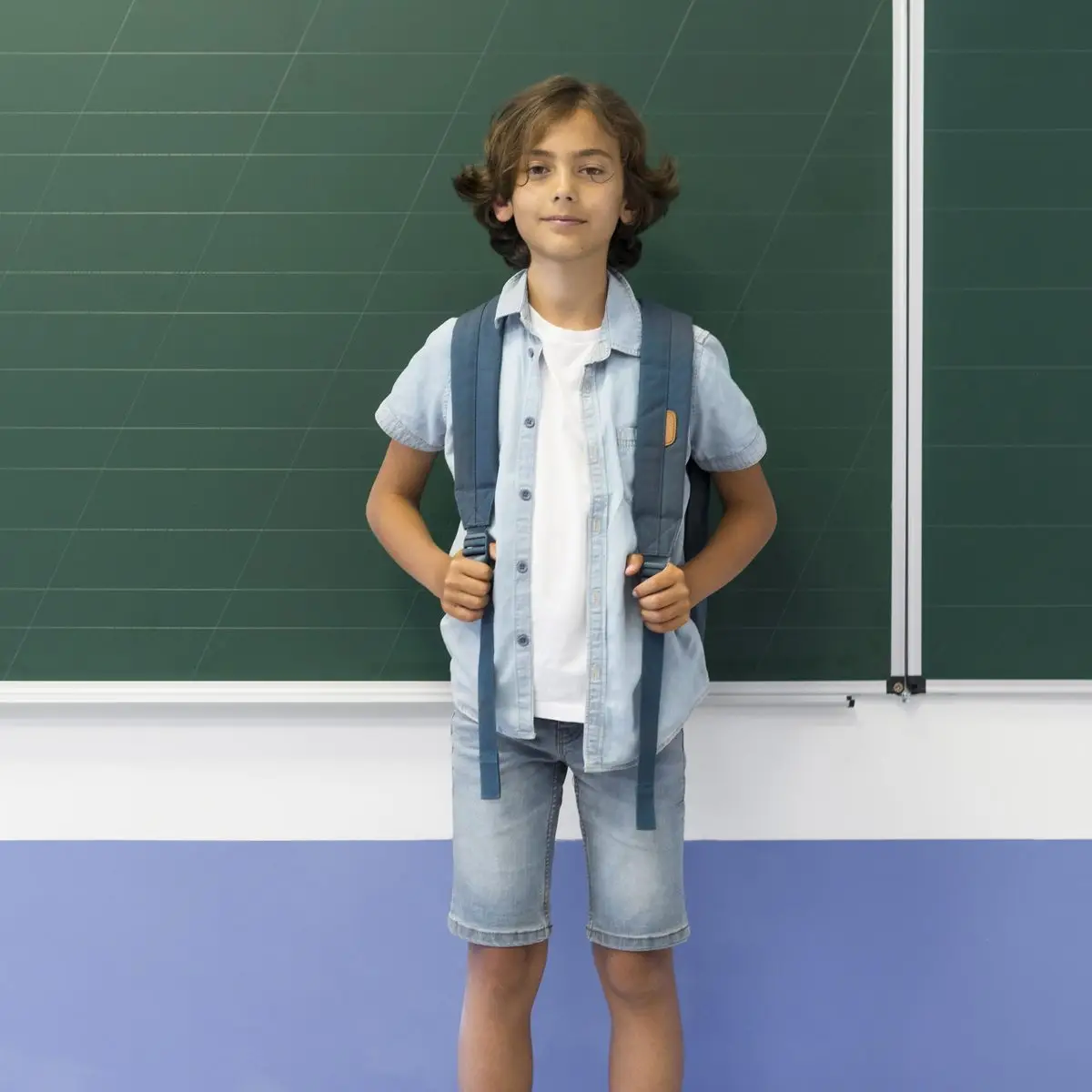 A schoolboy with a backpack standing in front of a chalkboard