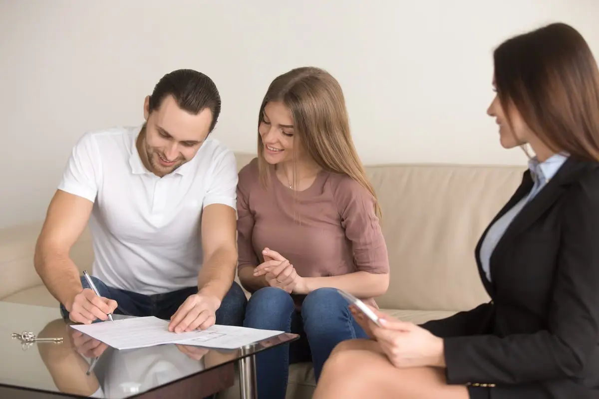 A couple signing a document on a coffee table while a lawyer looks on