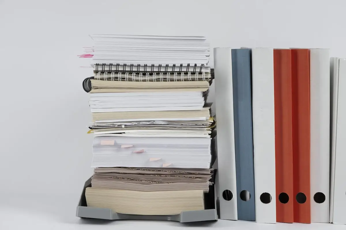 A tall stack of papers and binders on a desk