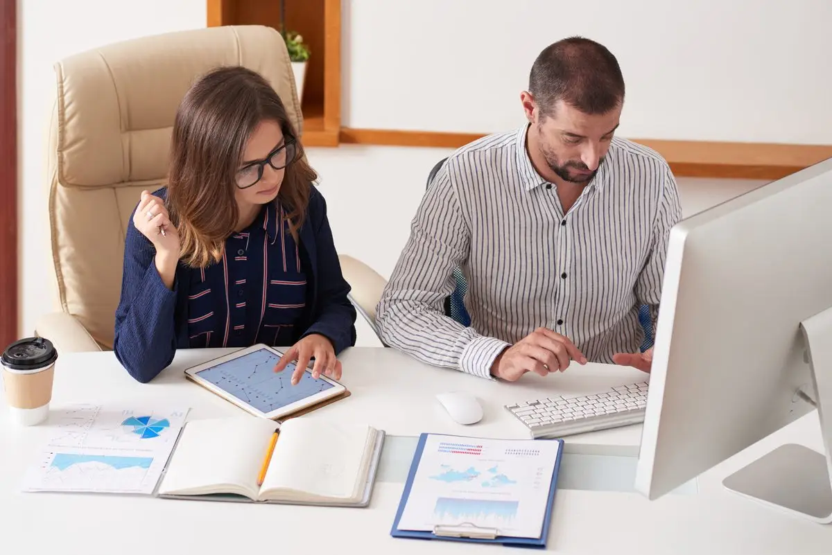 Two professionals reviewing financial figures on a tablet and in a notebook