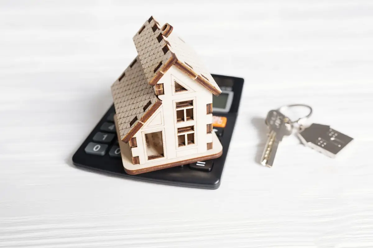 A small wooden house model and keys beside a calculator
