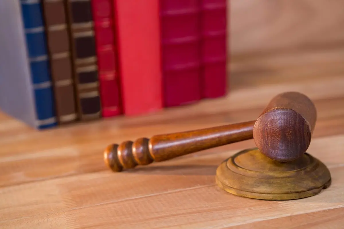 A judge's gavel resting on a stack of law books on a wooden desk