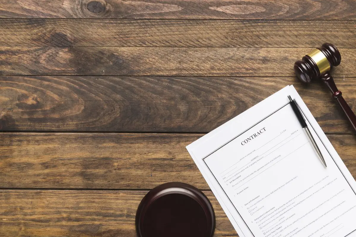 A contract with a pen and a judge's gavel on a wooden desk
