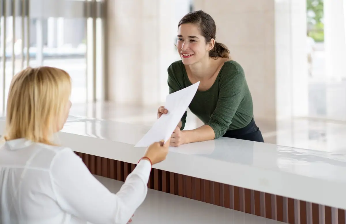 A front desk assistant handing a form to a visitor who is getting legal help