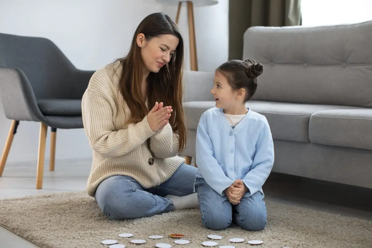 A mother and her young daughter kneel on a rug at home, playing a game together