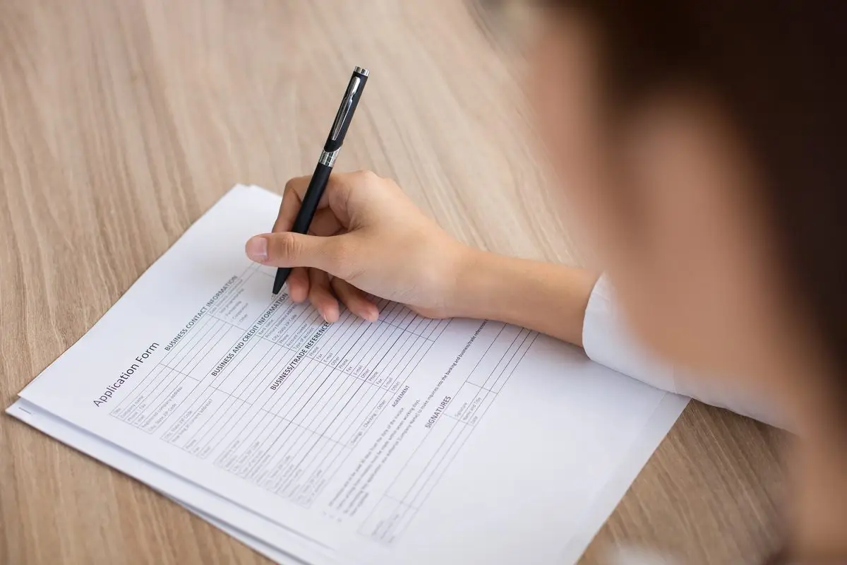 A hand completing an application form with a pen