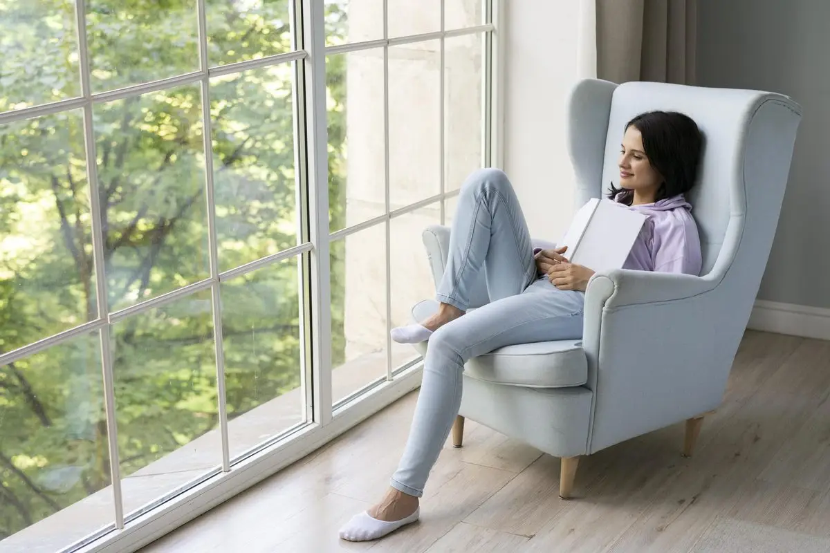A woman resting in an armchair beside a bright window at home