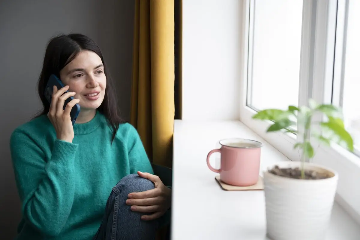 A woman speaking on her phone at home beside a sunny window