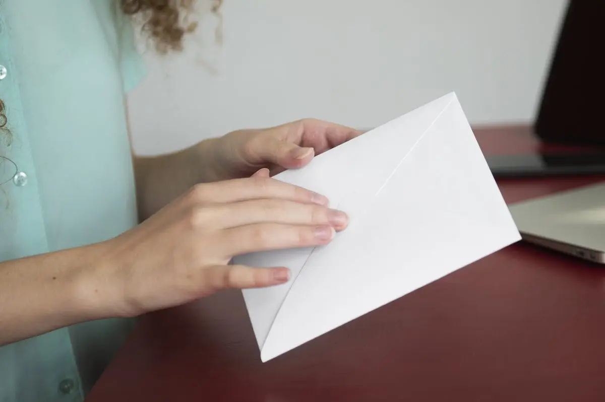A hand holding an envelope above a desk