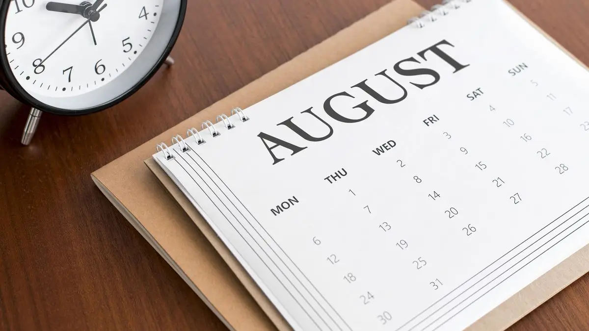 A desk calendar and a clock on a dark desk, marking the review date