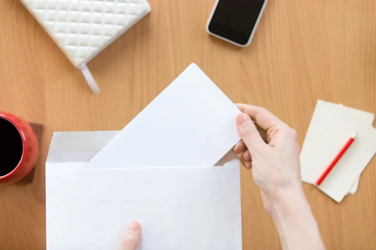 A hand holding a document taken out of an envelope