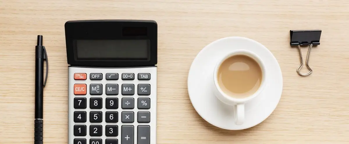 A calculator, a pen and a cup of coffee on a wood desk