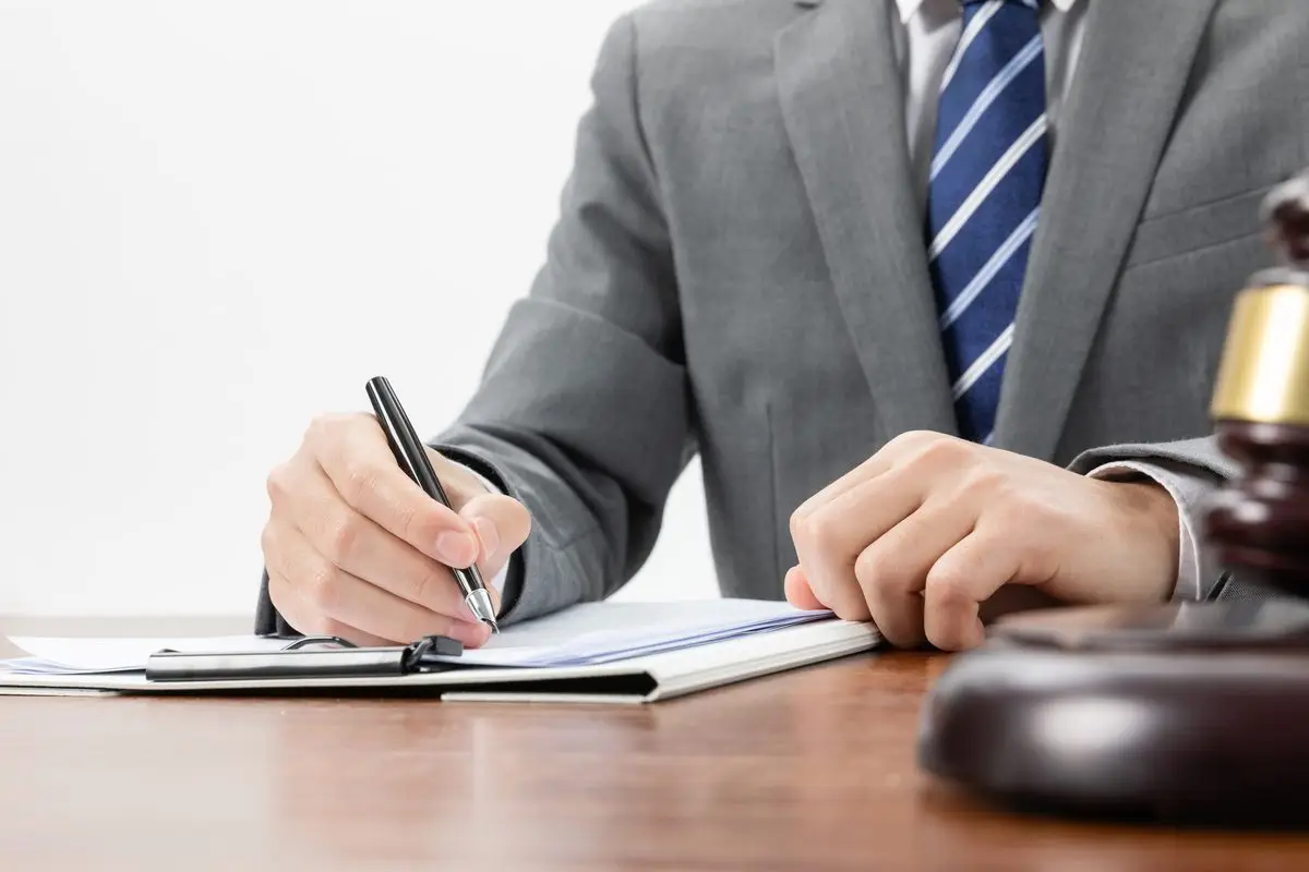 A hand signing official papers with a gavel in the corner