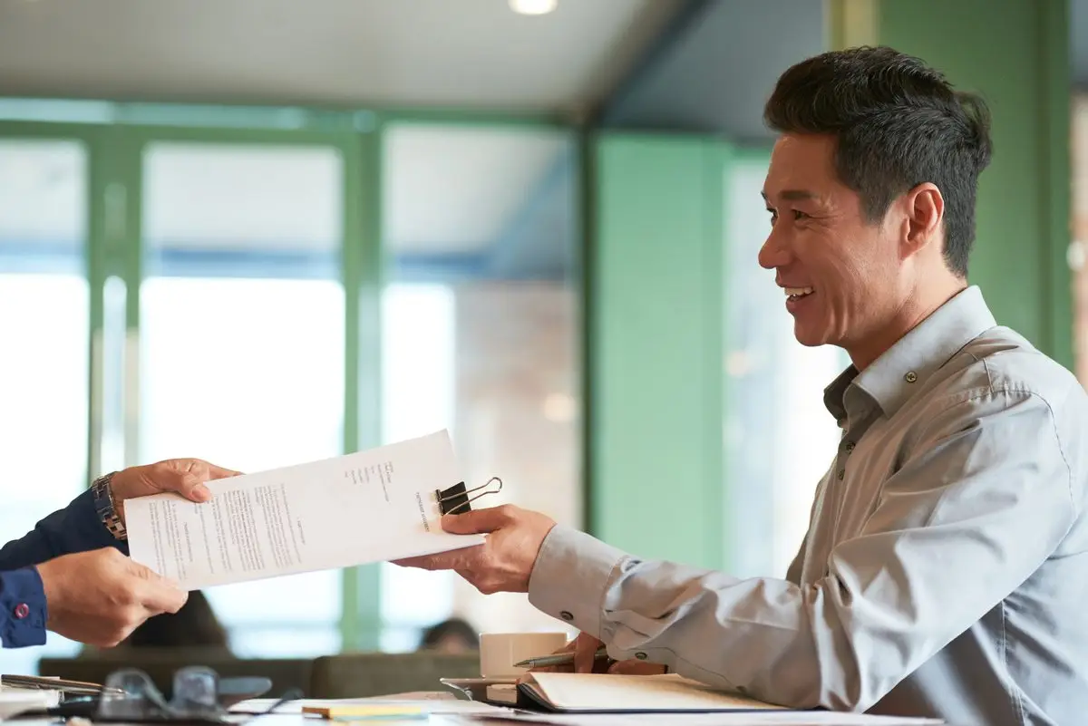 A man receiving a document handed across a desk