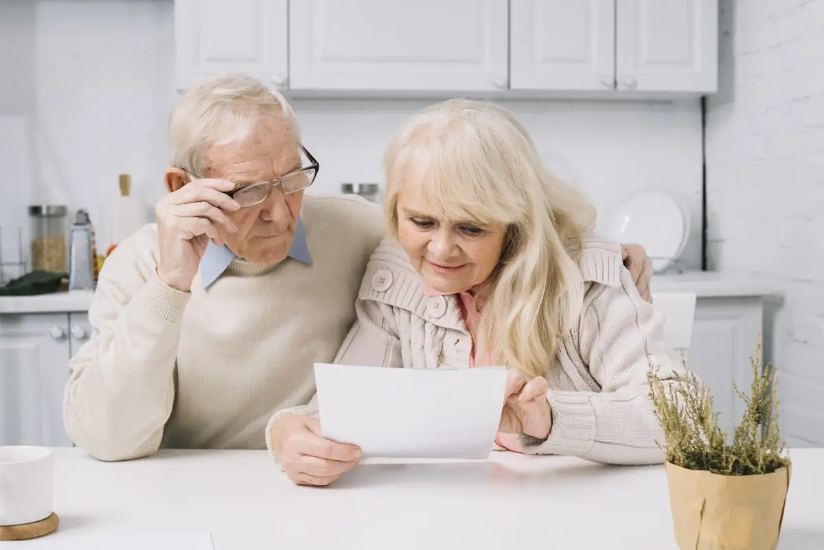 An older couple reading a document together at a kitchen table