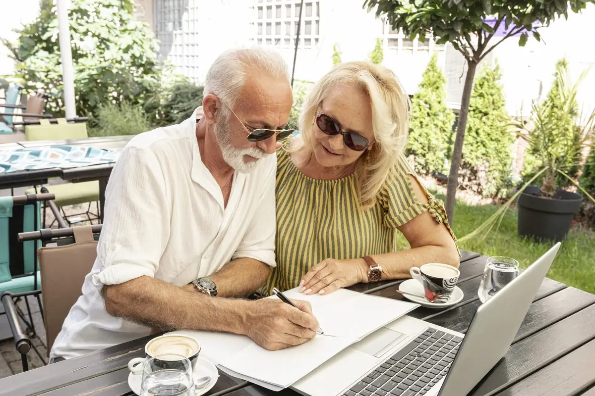 An older couple sitting at an outdoor table going over a document together