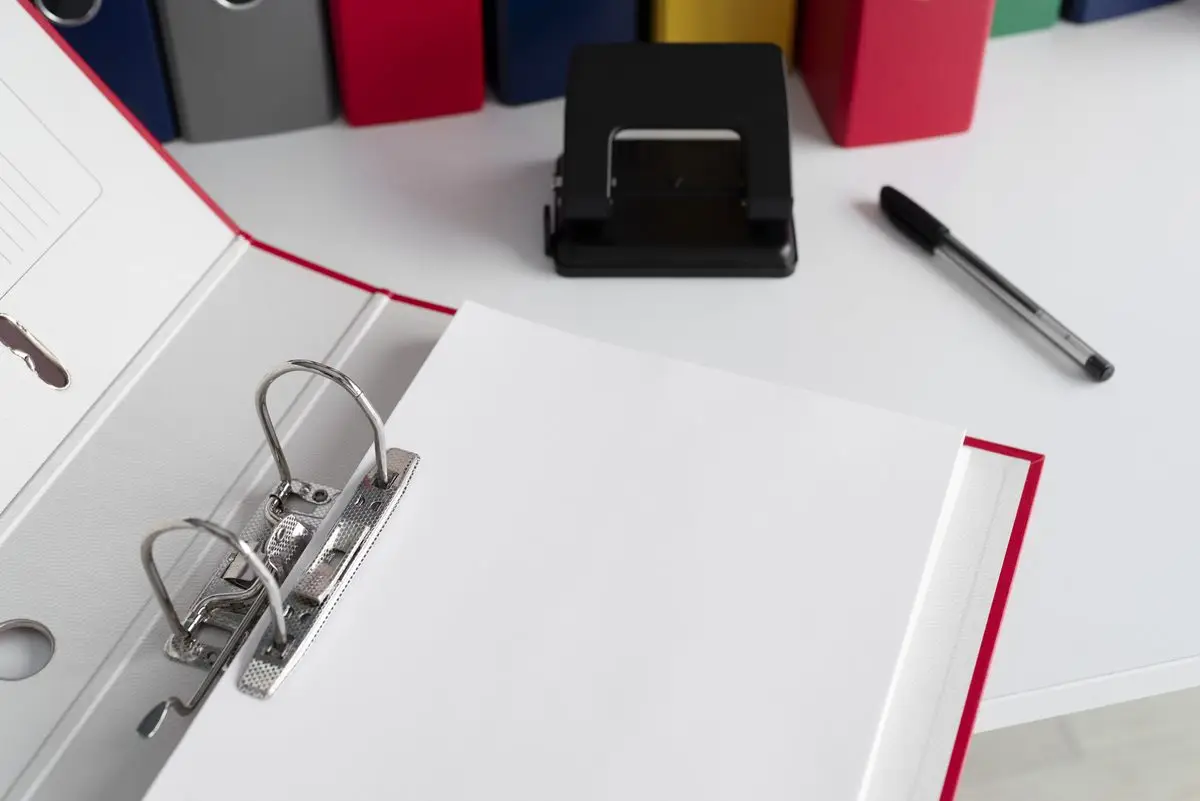 An open ring binder with blank forms and a pen on a white desk