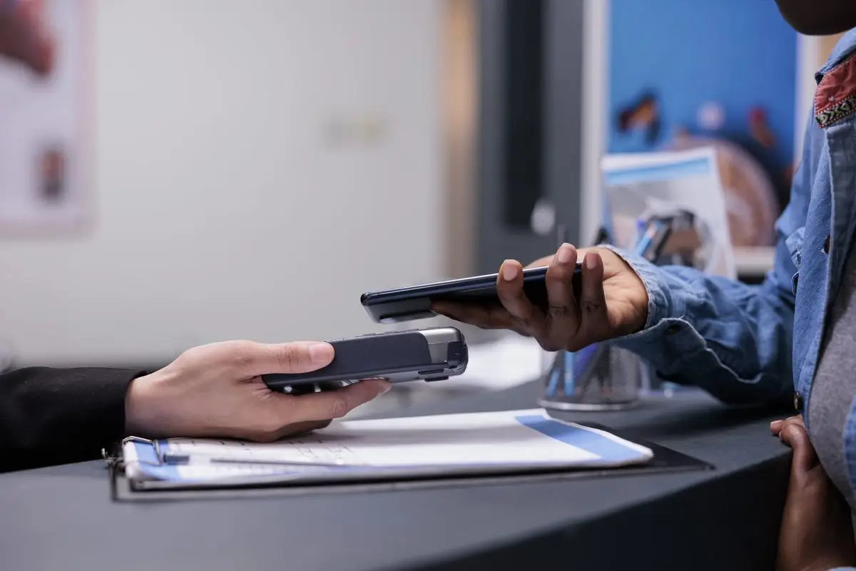 A person paying at a reception desk with a card terminal beside a form on a clipboard