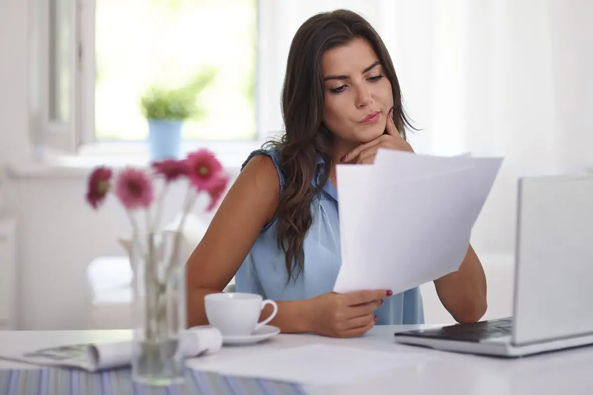 A woman at home reading through the pages of an agreement before she signs it