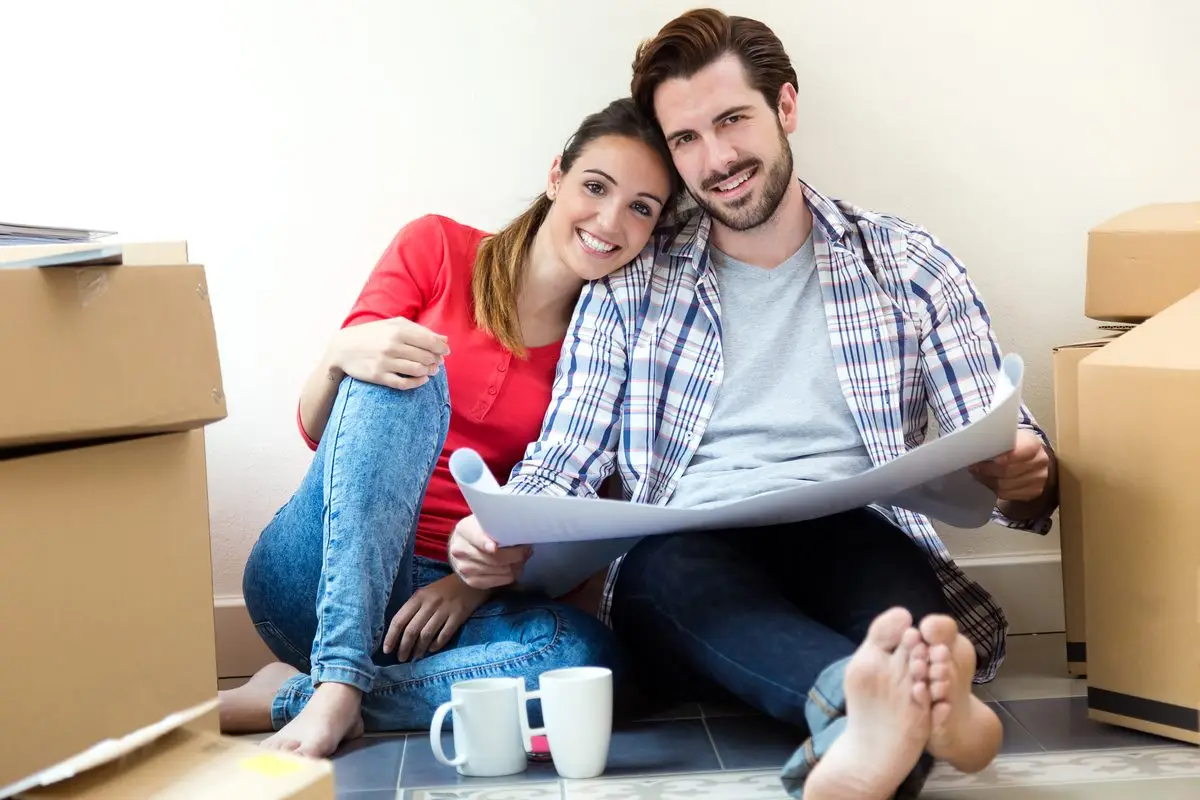 A couple sitting on the floor among moving boxes, looking over plans for their new home