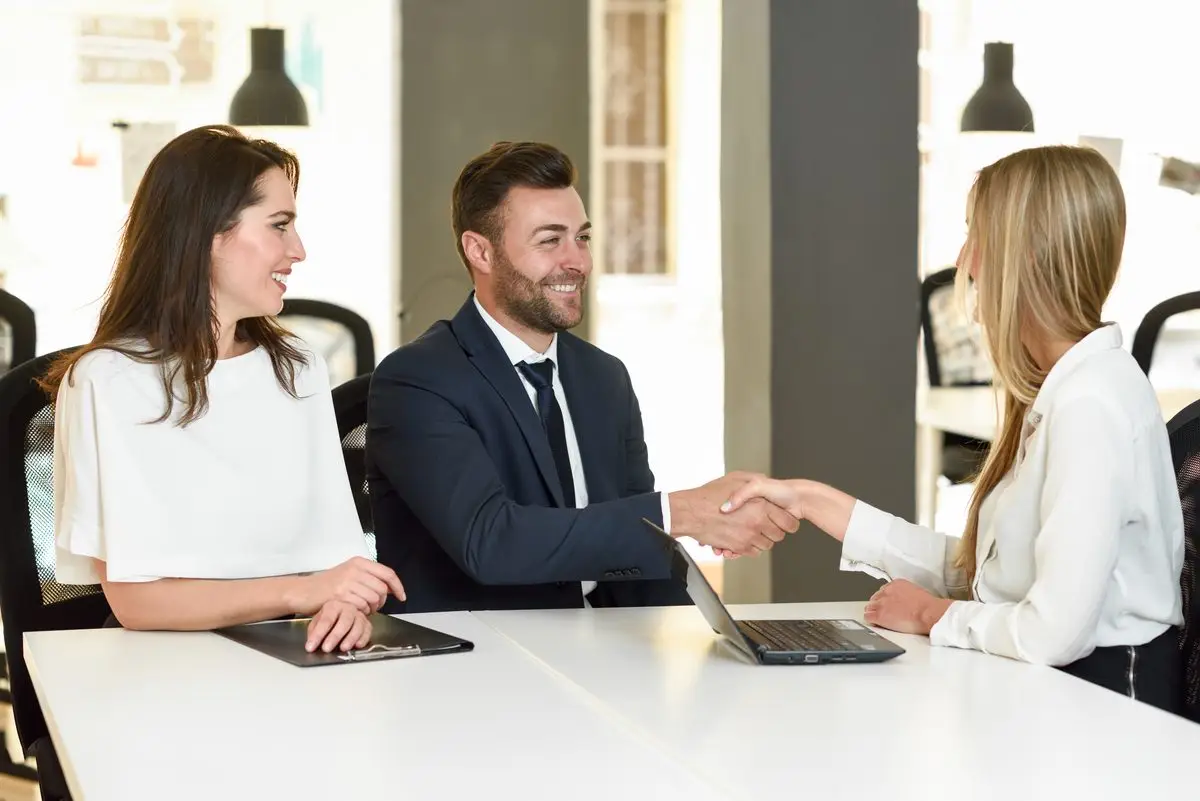 A couple sitting down for a meeting where an adviser shakes hands across the table