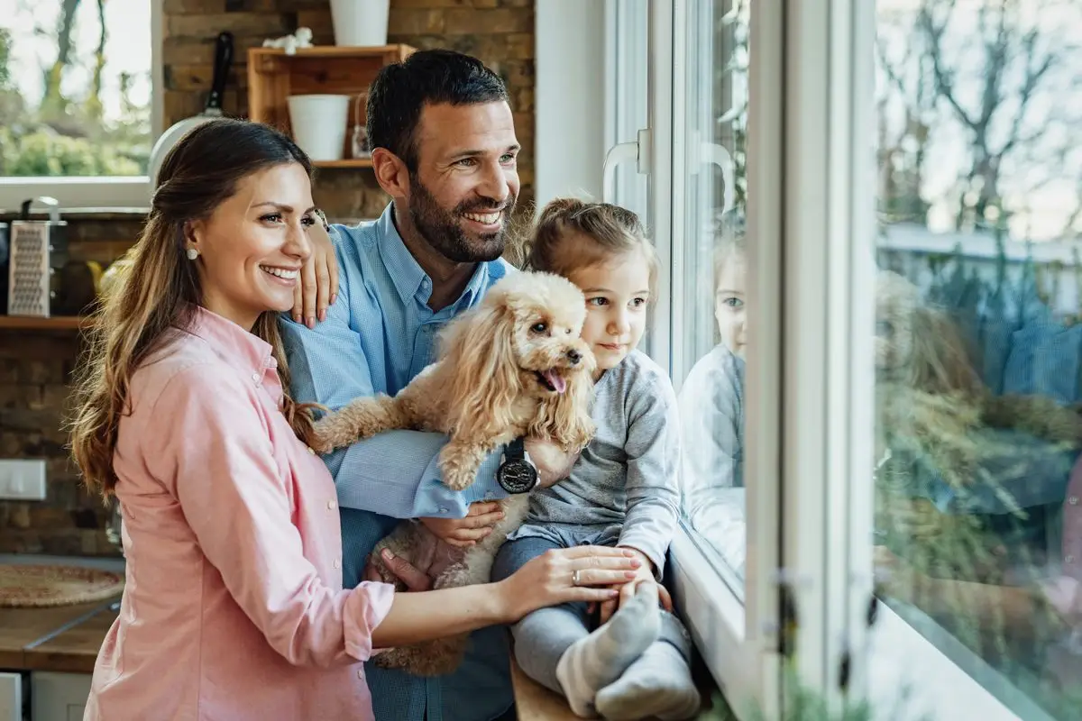 Two parents with their young child and dog at a sunny window at home
