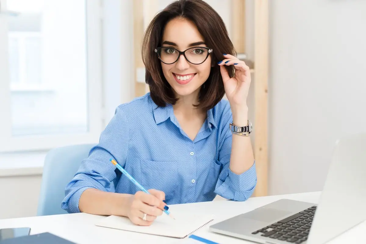 A smiling lawyer working at her laptop and notepad in a bright office
