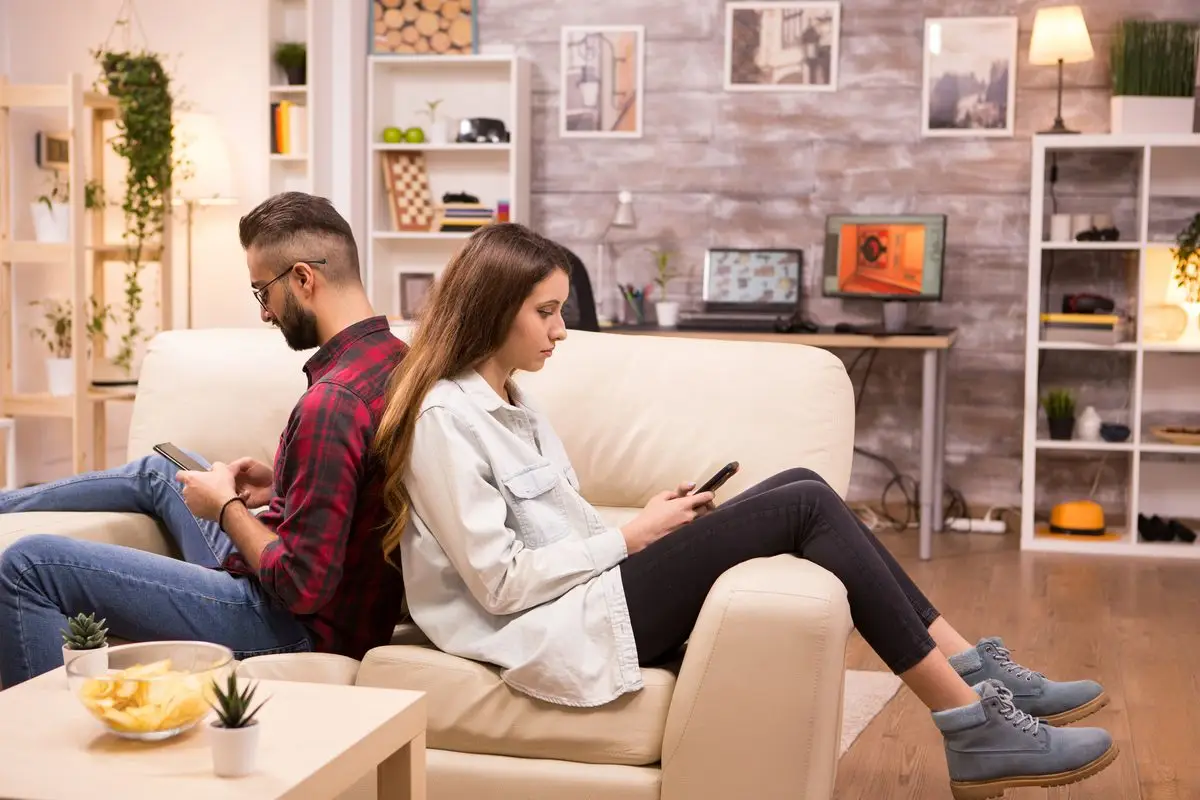A couple sitting back to back on a sofa, each looking at their phone after a disagreement