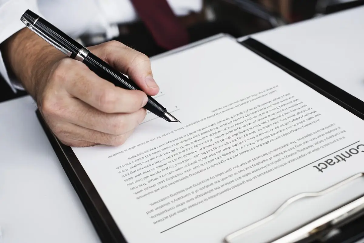 A hand signing a contract on a clipboard with a fountain pen