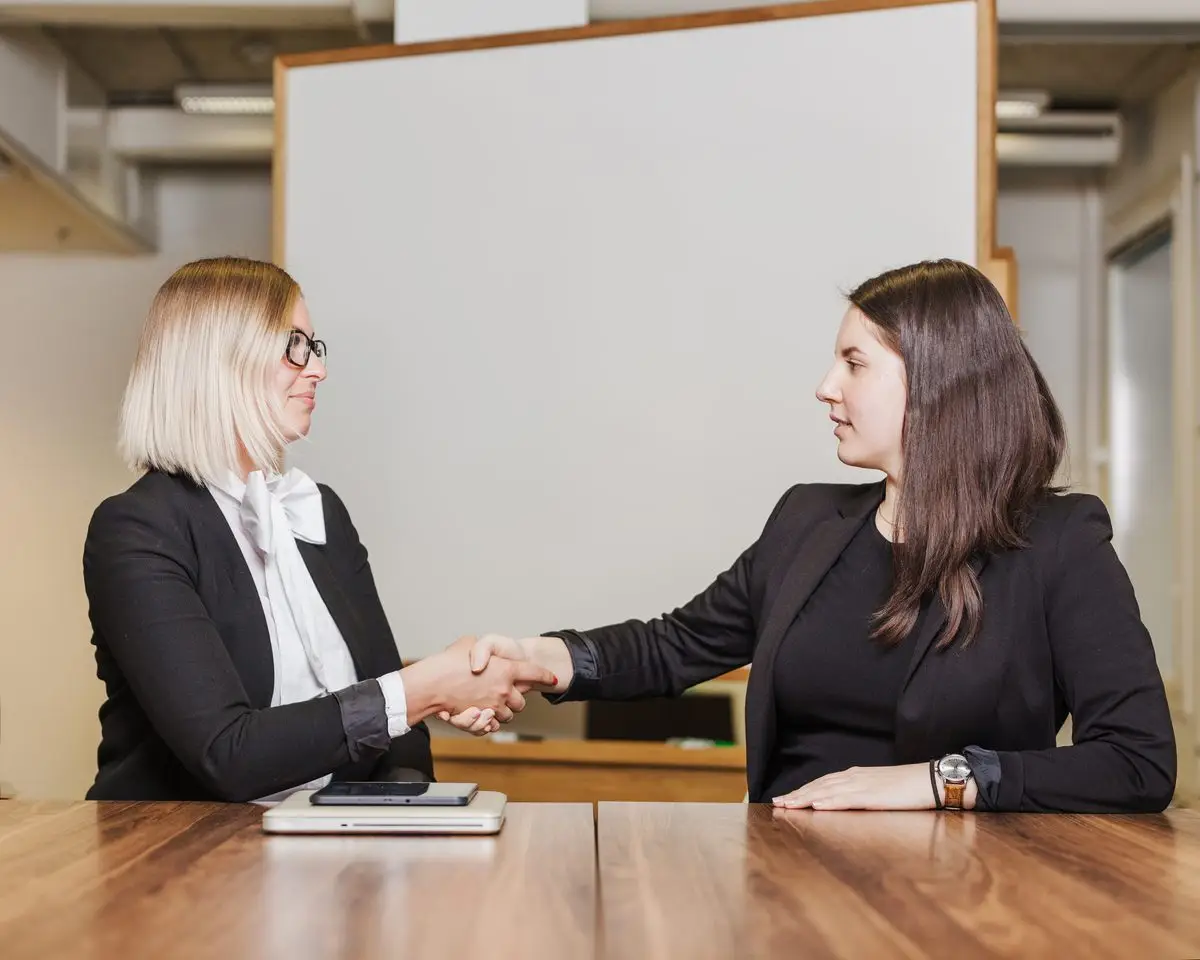 Two professionals shaking hands across a table after a meeting