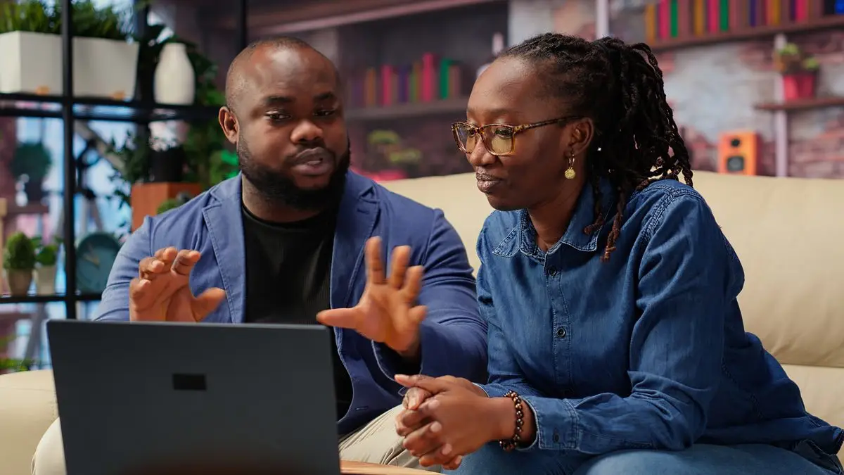A couple sitting on a sofa at home working through a video call on a laptop